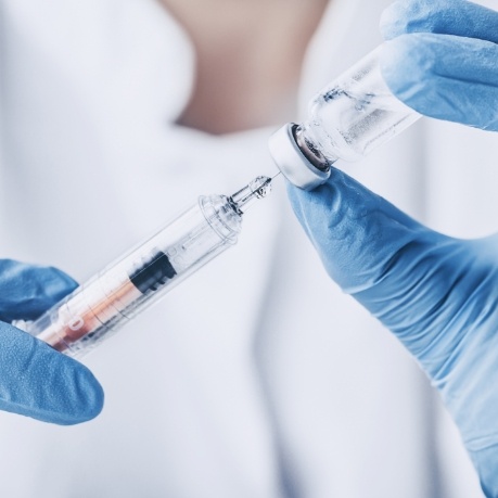 Dentist drawing syringe from vial of clear liquid