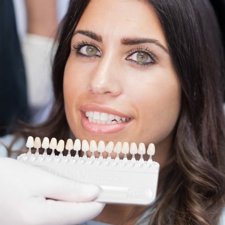 Dental patient smiling while dentist holds row of veneers