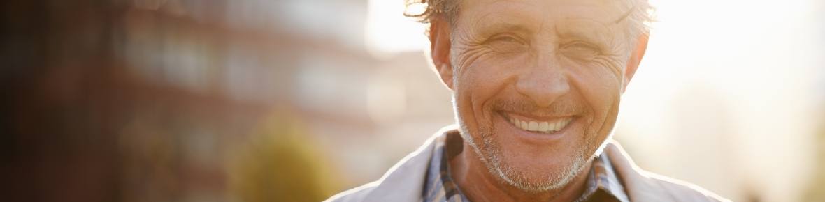 Older man smiling outdoors at sunset with dental implants in Cherry Hill