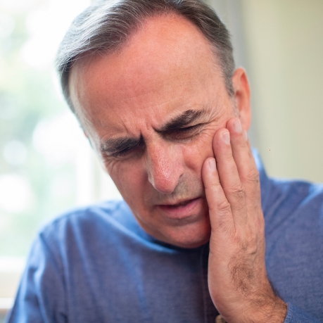 Man wincing and holding his cheek in pain