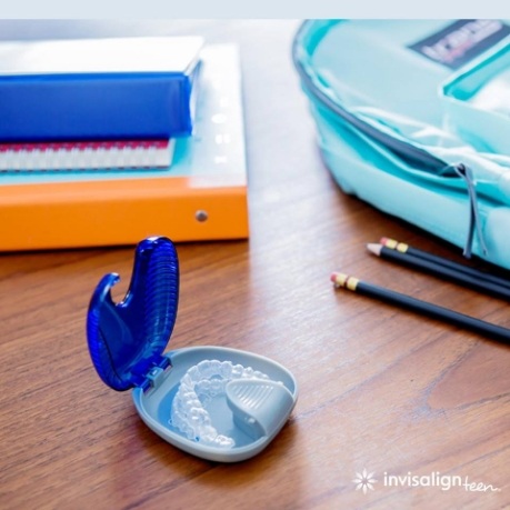 Invisalign aligners in their case on desk with school supplies
