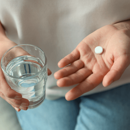 Person holding a white pill and a glass of water