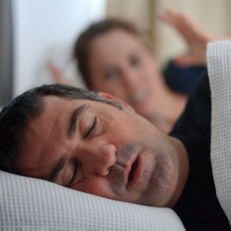 Frustrated woman laying in bed next to snoring man